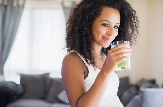 Pregnant woman smiles while drinking a green smoothie made with LuvBelly pregnancy safe greens powder